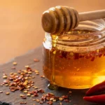 Hot honey recipe in glass jar with honey dipper showing golden spicy honey with chili flakes