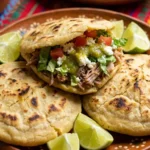 How to make gorditas recipe showing golden puffy corn cakes stuffed with carnitas meat lettuce and salsa on rustic plate
